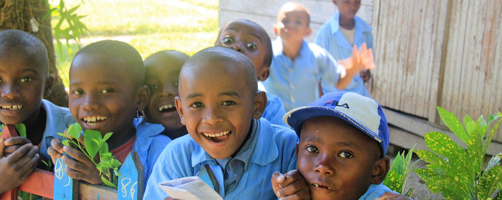 Kinder in Schuluniform im Schulgarten mit breitem Grinsen im Gesicht - glücklich in die Schule zu dürfen