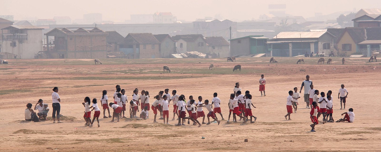 Kinder spielen in Schuluniform auf der weitläufigen Sandpiste in einer Schule am Rande der Hauptstadt, kurz Tana genannt