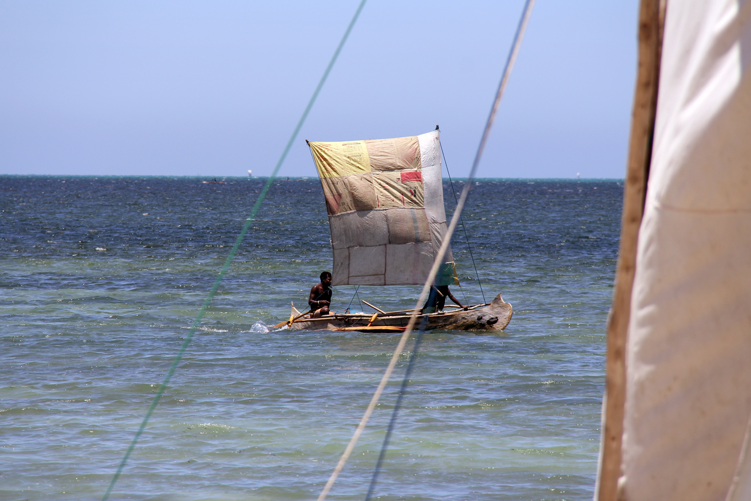 Ein Fischerboot - Einstamm, der mit einem aus Stofffetzen zusammengenähten Segel auf dem Meer zu seinen Fischründen segelt